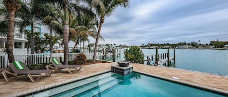 Relax by the serene pool overlooking the waterfront, surrounded by lush palm trees and modern architecture.