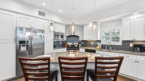 A modern kitchen with white cabinets, stainless steel appliances, a central island with seating, and pendant lighting.