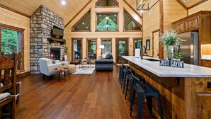 A spacious interior with a stone fireplace, a large kitchen with a stainless steel refrigerator, and a bar area. - HIGH Luxe MODERN 1+ Bedroom New Construction July 2022! (Broken Bow)