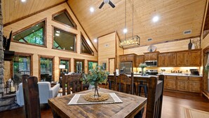 A spacious kitchen with wooden cabinets, a dining area with a wooden table, and large windows offering views of the outdoors. - HIGH Luxe MODERN 1+ Bedroom New Construction July 2022! (Broken Bow)