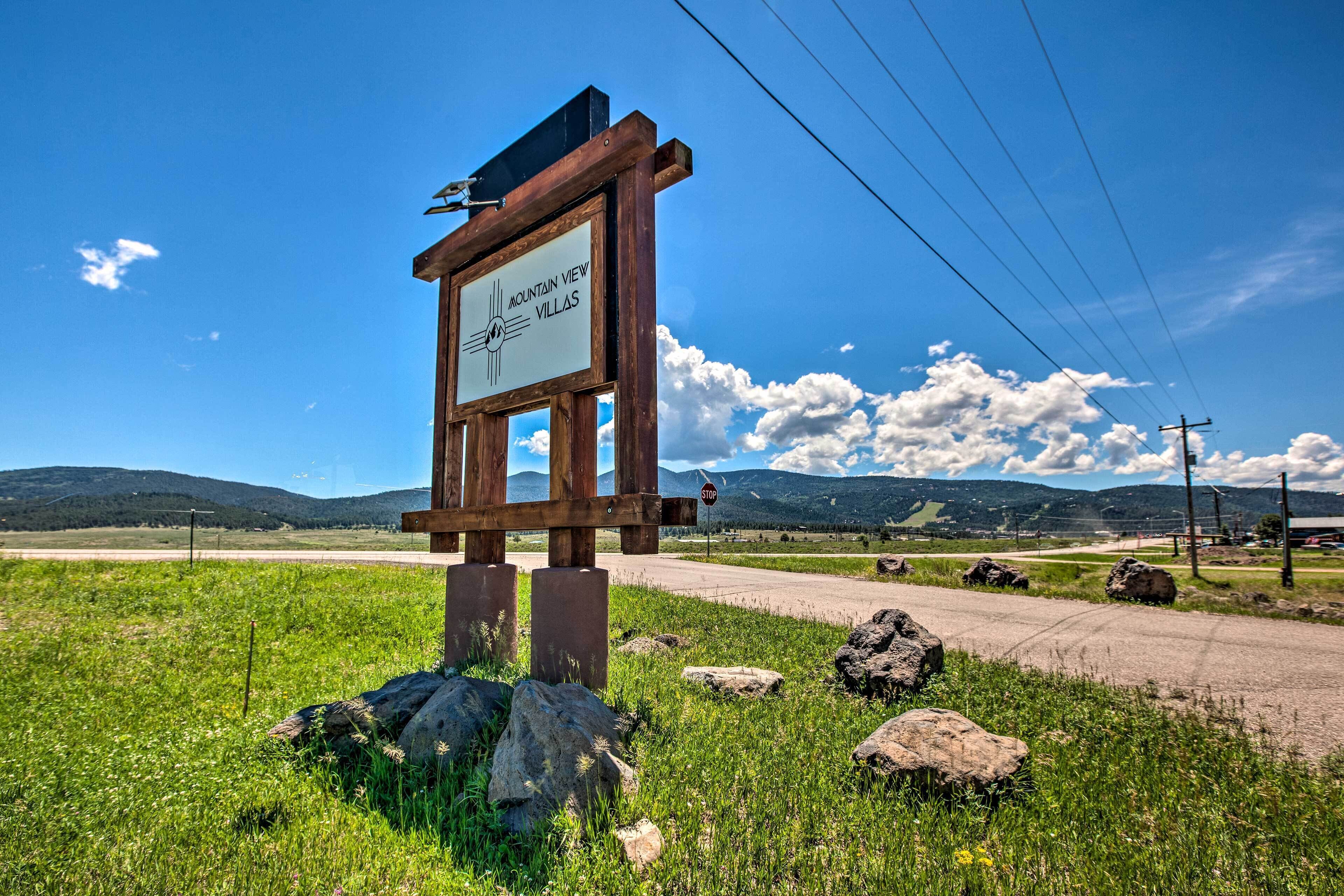 Un panneau en bois portant l’inscription « Mountain View Villas », avec en arrière-plan un ciel dégagé, un chemin de terre et des montagnes lointaines.