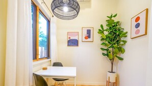 A small dining area with a white table and black chairs, a large potted plant, and abstract art on the wall.