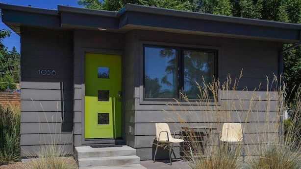 A modern house with a green door, number 1056, and a small patio with two chairs.