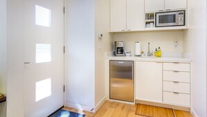 A compact kitchen with white cabinets, a microwave, a coffee maker, and a mini-fridge.