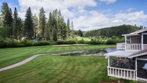 Ein Golfplatz mit Teich, umgeben von dichter Baumgruppe und einem Gebäude mit Balkon.