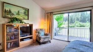 Ein Zimmer mit einer großen Schiebeglasdoor zum Balkon, einem Bücherregal, einem Fernseher und einem Sessel.