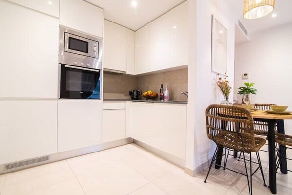 A modern kitchen with white cabinetry, a built-in oven, and a dining area with wicker chairs and a table.