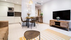 A modern living room with a sofa, a dining table with chairs, a TV on a wooden stand, and a kitchen area with appliances. - Luxury modern apartment with exceptional views! (Gibraltar)