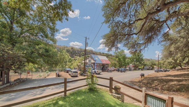 A rural road with a wooden fence, a small building with a red roof, and a stop sign. - Lil Kahuna Rr 7465 1 Bedroom Home by RedAwning (New Braunfels)