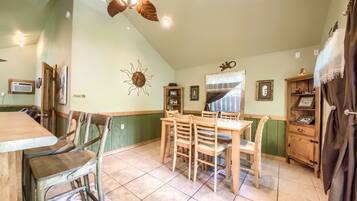 A dining area with a wooden table and chairs, a ceiling fan, and a window with curtains.