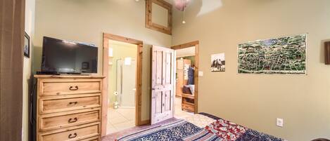 A bedroom with a wooden dresser, a television on top, a ceiling fan, and a quilt on the bed.