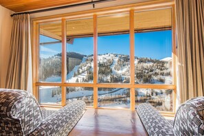 A room with a large window offering a view of a snowy mountain landscape.