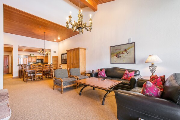 A spacious living area with a dining table, chairs, a sofa, and a chandelier.