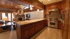 A spacious kitchen with wooden cabinets, a large island, a stone fireplace, and a modern stove. - Flagstaff Two Bedroom 2 Apartment Hotel by RedAwning (Park City)