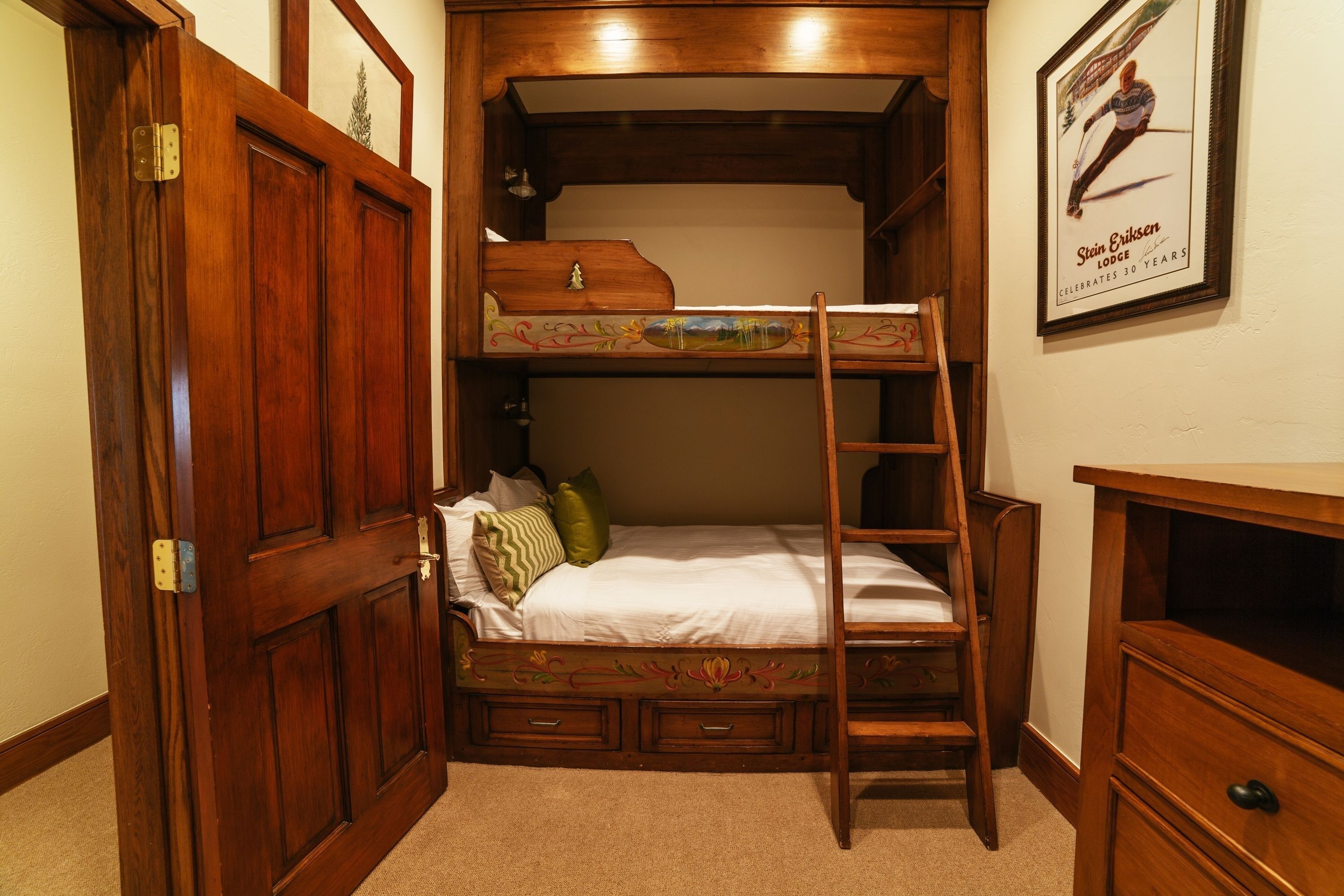 A compact room with a bunk bed, a ladder, a dresser, and a framed picture on the wall.