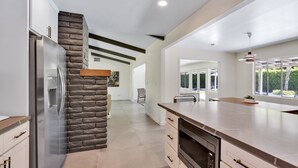 A modern kitchen with a stone accent wall, stainless steel appliances, and a large island. - Sunset Ranch - Updated midcentury home with Pool & Spa! (Palm Springs)
