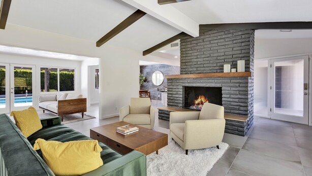 A modern living room with a stone fireplace, a green sofa, and a pool view. - Sunset Ranch - Updated midcentury home with Pool & Spa! (Palm Springs)