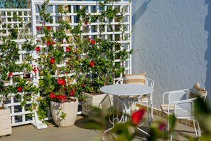 An outdoor patio with white metal chairs and a table, surrounded by potted plants and a white lattice structure. - Nari Lunder Agro-Tourism (Farkë)