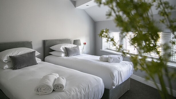 A modern hotel room with two beds, a large window with blinds, and a ceiling light. - A spacious and stylish 2 bedroom, 2 bathroom duplex apartment (Grassington)