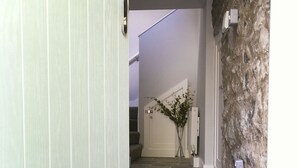 A hallway with a green door, a doormat with "hello" written on it, and a stone wall. - A spacious and stylish 2 bedroom, 2 bathroom duplex apartment (Grassington)
