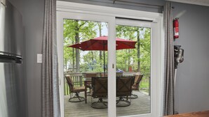 A sliding glass door leading to an outdoor deck with a table and chairs, a red umbrella, and a fire extinguisher mounted on the wall. - ❤️ Spacious Island Cottage at Indian Lake ❤️ (Huntsville)