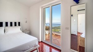 A bedroom with a bed, a nightstand, a window, and a sliding door leading to a balcony. - Villa La Luce: Town Centre, Sea Views, Pool & Concierge by Feeling Italy (Massa Lubrense)