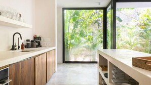 A modern kitchen with wooden cabinets, a white countertop, and a large window with a view of lush greenery. - Casa Areca, 4 bed/4.5 bath World Renowned Design Villa, Pool, Rooftop, 24/7Guard (Tulum)