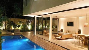A modern outdoor pool area with a wooden deck, seating, and a glass-enclosed lounge area. - Casa Areca, 4 bed/4.5 bath World Renowned Design Villa, Pool, Rooftop, 24/7Guard (Tulum)