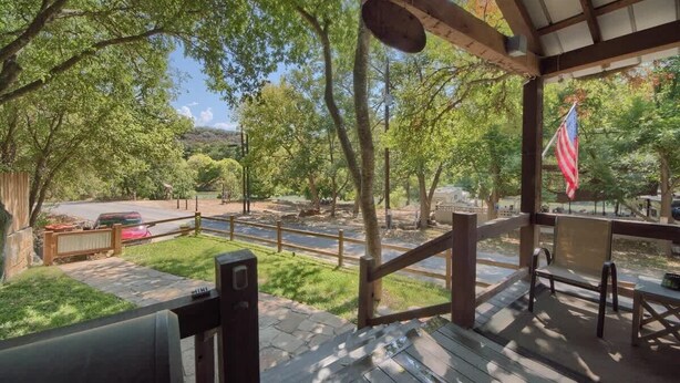 A covered outdoor area with a view of a road and trees, a flag, and a bench. - RR 7465 Lil Kahuna (New Braunfels)