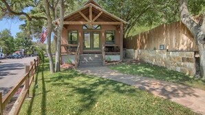 A wooden cabin with a porch, a flag, and a stone wall. - RR 7465 Lil Kahuna (New Braunfels)