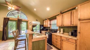 A kitchen with wooden cabinets, a stove, a sink, and a dining area with a chair. - RR 7465 Lil Kahuna (New Braunfels)