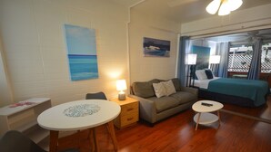 Ein gemütliches Zimmer mit Holzboden, einem runden Esstisch, einer Couch und einem Bett mit Blick auf das Meer durch ein Fenster.