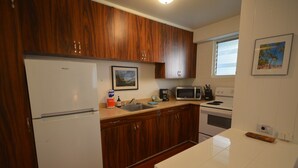 Eine Küche mit Holzschränken, einem weißen Kühlschrank, einer Mikrowelle, einem Spülbecken und einem Herd.