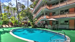 Ein Swimmingpool, umgeben von Grünflächen, mit einem mehrstöckigen Gebäude und Balkonen.