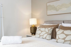 A neatly made bed with a white duvet, a gold-toned lamp, and patterned pillows on a white nightstand. - The Old Office No. 4 (Darlington)