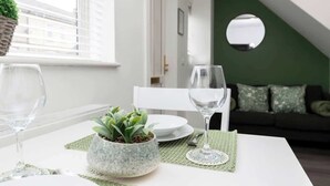 Ein Essbereich mit Tisch für zwei Personen, einem Blumentopf und einer grünen Wand im Hintergrund.