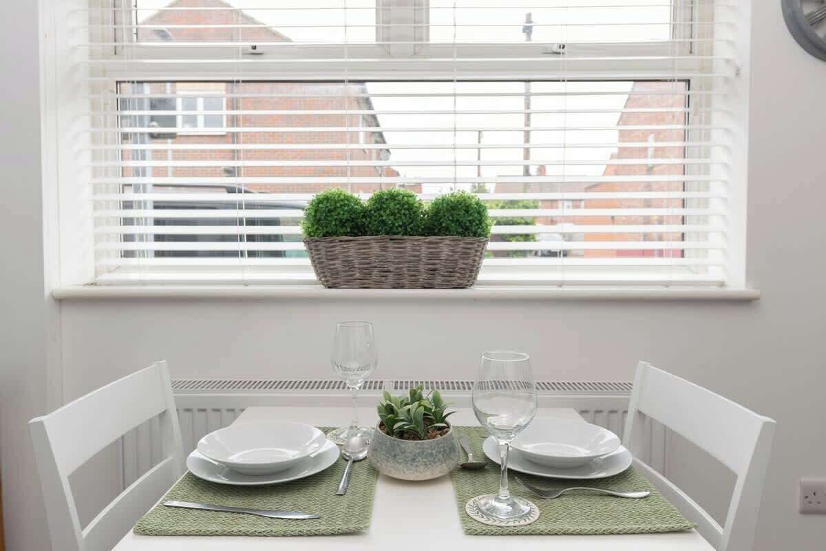 A dining table set for two with white chairs, a small potted plant, and two wine glasses.