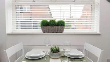 A dining table set for two with white chairs, a small potted plant, and two wine glasses.