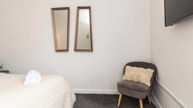 Ein Hotelzimmer mit einem Bett, einem Sessel, zwei Wandspiegeln und einem an der Wand montierten Flachbildfernseher.