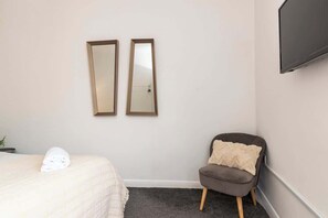 Ein Hotelzimmer mit einem Bett, einem Sessel, zwei Wandspiegeln und einem an der Wand montierten Flachbildfernseher.