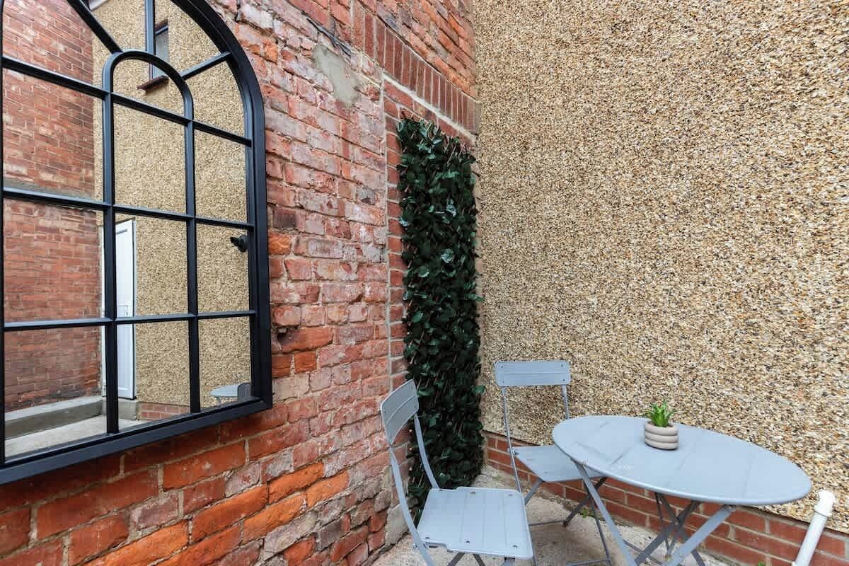 A brick wall with a window, a metal chair, and a table with a plant.
