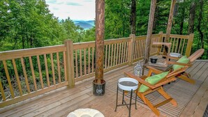 Une terrasse en bois offrant une vue sur une forêt et des montagnes, une table avec des chaises et un seau.