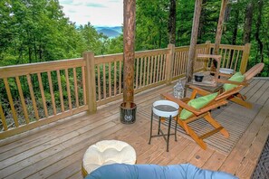 Une terrasse en bois offrant une vue sur une forêt et des montagnes, une table avec des chaises et un seau.