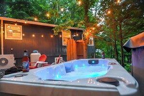A hot tub with a wooden deck, surrounded by trees and string lights.