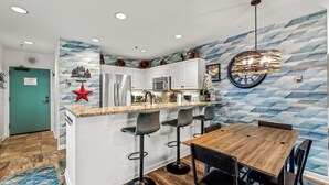 Uma cozinha moderna com área de bar, com uma mesa de jantar de madeira, banquetas e um pendente de teto exclusivo.