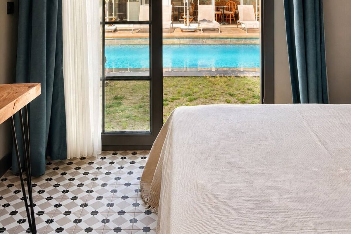 A hotel room with a bed, a view of a swimming pool, and a patio area.