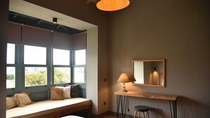 Ein Zimmer mit einem großen Fenster, einer hölzernen Bank, einem Schreibtisch mit Lampe und einem Spiegel.