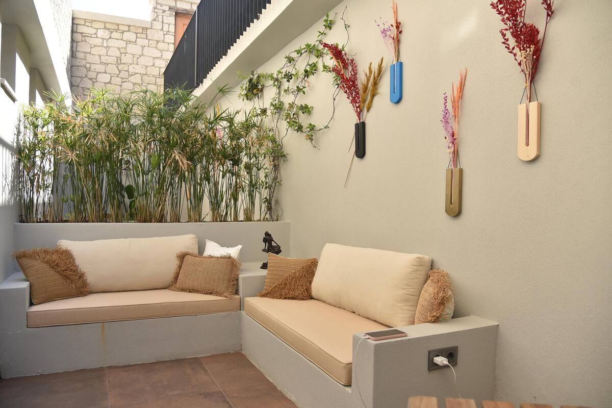 A corner seating area with a cushioned bench, a small table, and a wall-mounted vase with dried plants.