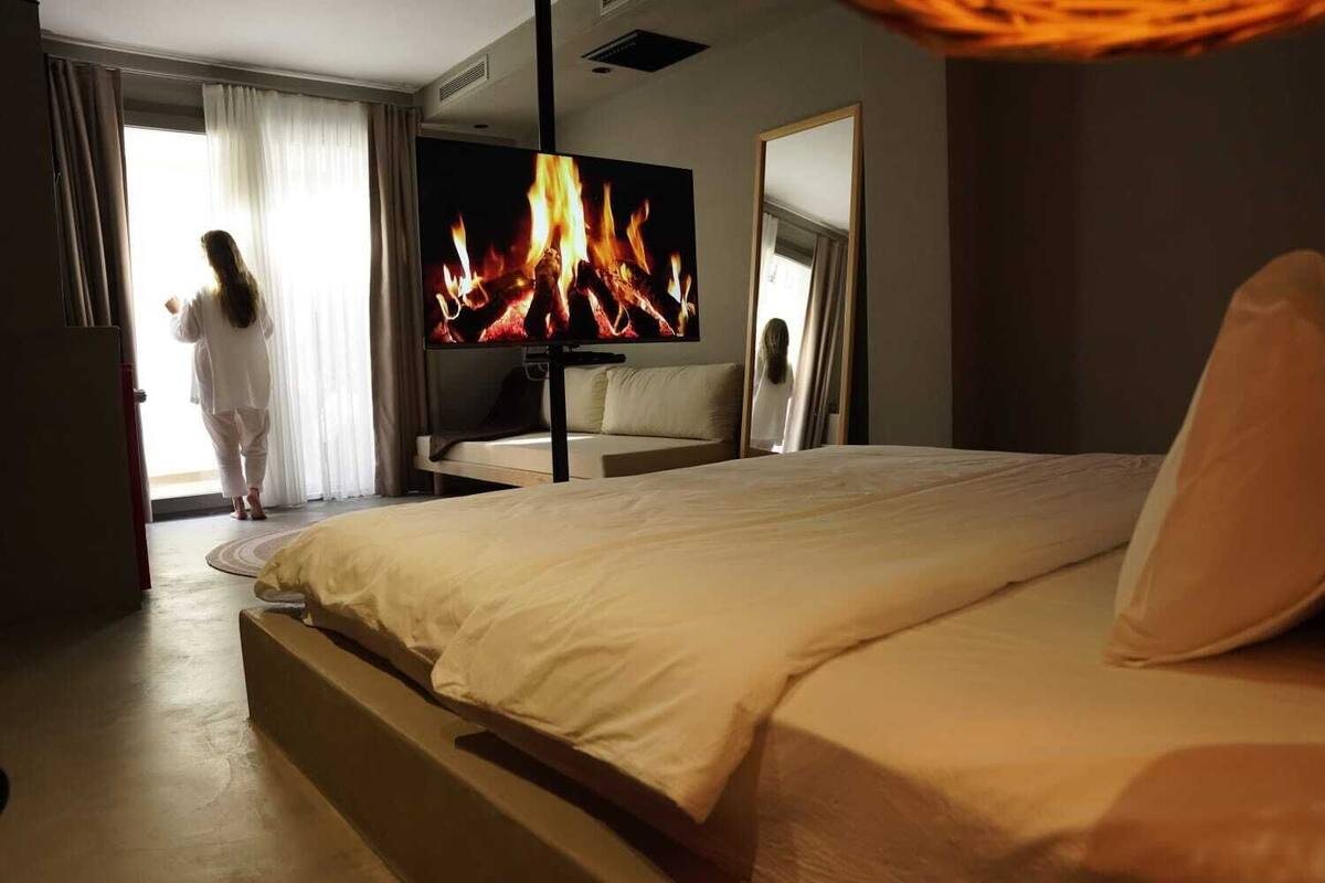 A hotel room with a bed, a TV displaying a fire, and a window with curtains.