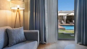Ein modernes Hotelzimmer mit einer Couch, einer Stehlampe und Blick auf einen Pool sowie einen Sitzbereich im Freien.